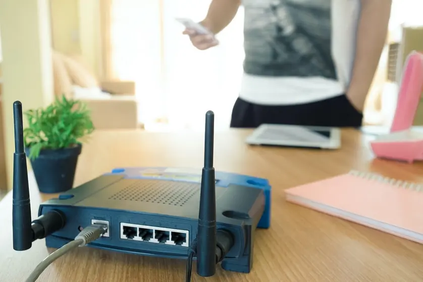 closeup of a wireless router and a young man using a smartphone  on living room at home with a window in the background
