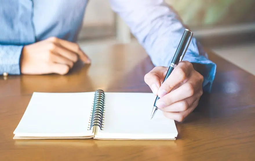 Business woman hand is writing on notepad with pen in office.
