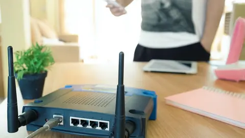 closeup of a wireless router and a young man using a smartphone  on living room at home with a window in the background
