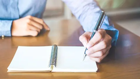 Business woman hand is writing on notepad with pen in office.